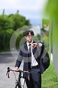 Businessman checking time on his wrist watch and commuting to work with bicycle.