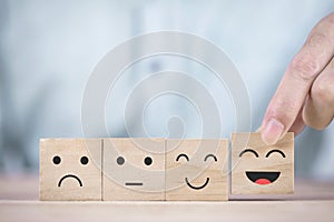 Businessman chooses a smiley face happy symbol on wooden block , Services and Customer satisfaction survey concept