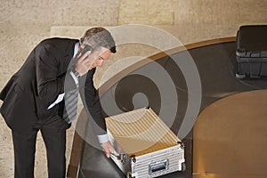 Businessman Claiming Suitcase At Luggage Carousel In Airport