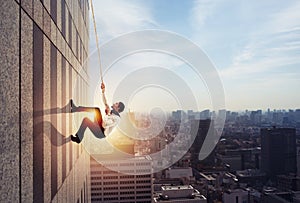 Businessman climbs a building with a rope. Concept of determination