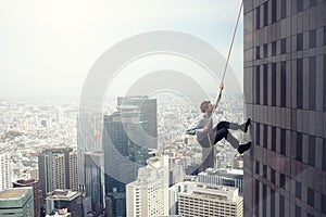 Businessman climbs a building with a rope. Concept of determination