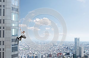 Businessman climbs a building with a rope. Concept of determination.