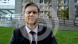 Businessman with closed eyes relaxing on green lawn near office center, rest