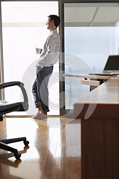 Businessman With Coffee Cup Leaning On Sliding Door