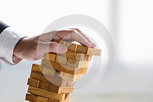 Businessman collapsing stacked tower wood block by hand as failure or bankrupt project. Business organization and company