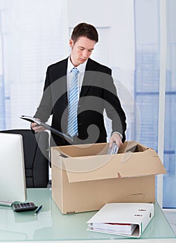 Businessman collecting office supply in cardboard box at desk