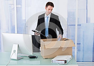 Businessman collecting office supply in cardboard box at desk