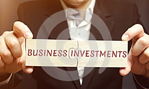 Businessman collects wooden puzzles with the words business investments. Increase capital. Investing your assets in your own or