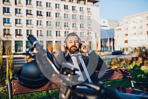 Businessman commuter with bicycle sitting on bench in city, listening to music.