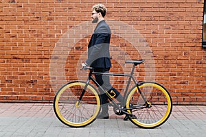 Businessman commuter with bicycle walking home from work in city agaist street brick wall