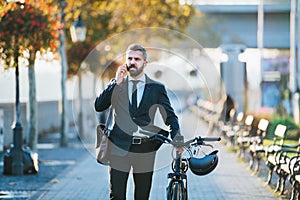 Businessman commuter with bicycle walking home from work in city, using smartphone.