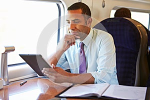 Businessman Commuting On Train Using Digital Tablet