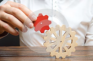 Businessman connects a small red gear to a large gear wheel. Symbolism of establishing business processes and communication.