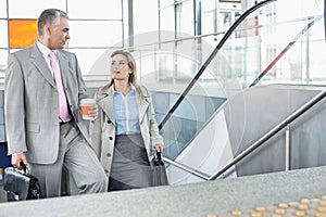 Businessman conversing with female colleague while walking up stairs in train station