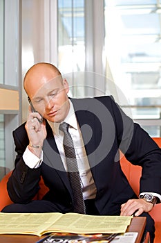 Businessman conversing on mobile phone while reading newspaper