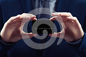 Businessman in costume and necktie hold credit card, close up. Black background concept of e-business shopping