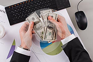 Businessman counting money with computer and papers at office.