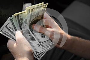 A businessman counting money. Man`s hands with dollars in a car on a blurred background. Financial business concept.