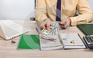 Businessman counting money at office desktop with laptop and empty notepad. Bribery concept