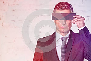 Businessman covering eyes with paper against white brick wall at office