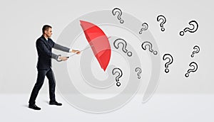 A businessman covering himself with an open red umbrella from many black drawn question marks.