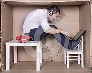 Businessman in a cramped cardboard office trying to focus on his work
