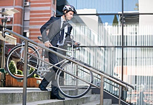 Businessman in crash helmet carrying bicycle down steps