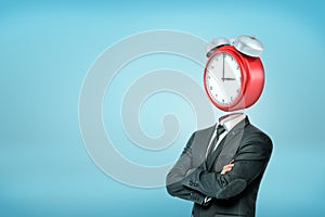 A businessman with crossed arms stands in half-turn with a large red alarm clock instead of his head.