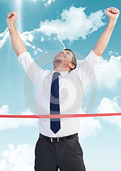 Businessman crossing finish line with arms up against sky and cloud