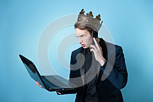 businessman with a crown on his head uses a laptop and a phone.