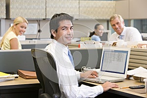 Businessman in cubicle with laptop smiling