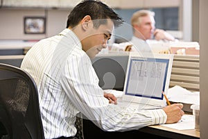 Businessman in cubicle with laptop writing photo