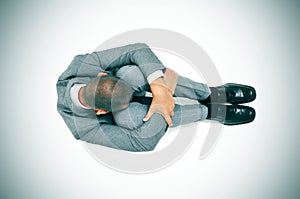 Businessman curled up in the floor with his head between his kne