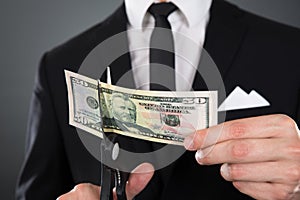 Businessman cutting dollar bill with scissors