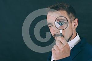 Businessman on a dark background with a magnifying glass in his hand