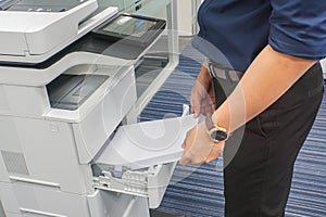 Businessman in dark blue shirt insert A4 paper sheet into office printer tray