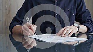 Businessman in dark blue t-shirt is signing contract at desk. Close-up of a male executive signing a legal document on a