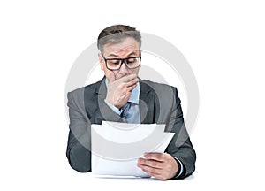 Businessman in a dark jacket and glasses reads paper documents covering his mouth with his hand, isolated on a white background.