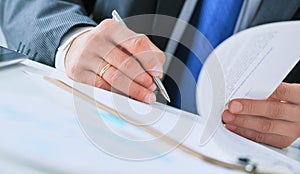 Businessman in dark suit sitting at office desk signing a contract with shallow focus on signature.