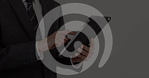 Businessman in dark suit and striped necktie holding tablet computer and tapping screen in studio