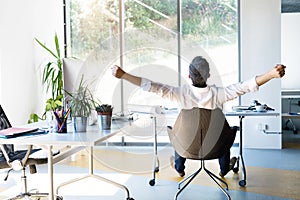 Businessman at the desk in his office stretching arms.