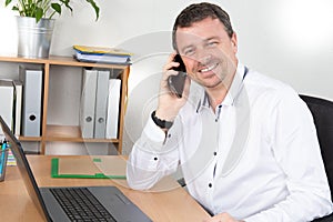 Businessman at desk in pghone in office with laptop computer