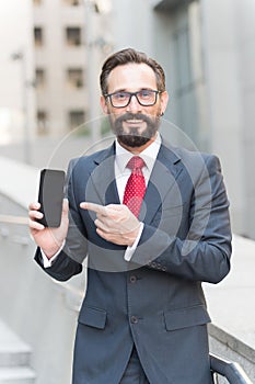 Businessman and digital gadget. Portrait of smiling businessman pointing finger at blank screen mobile phone