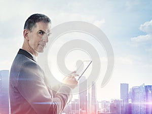 Businessman with digital tablet and blurred city on horizon