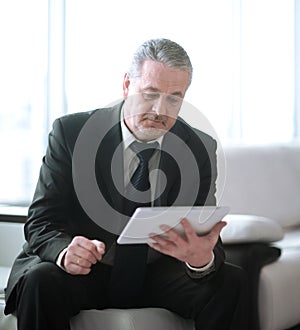 Businessman with digital tablet sitting on sofa in office