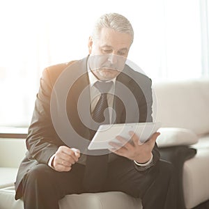 Businessman with digital tablet sitting on sofa in office