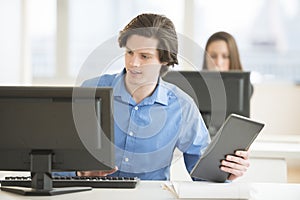 Businessman With Digital Tablet Using Computer At Desk