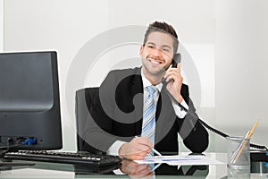 Businessman discussing over documents on telephone at desk