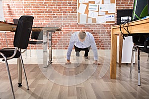 Businessman Doing Push Up In Office