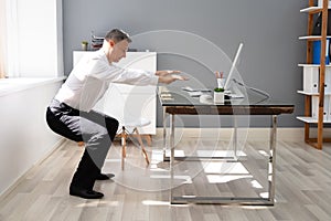 Businessman Doing Squats Exercise In Office